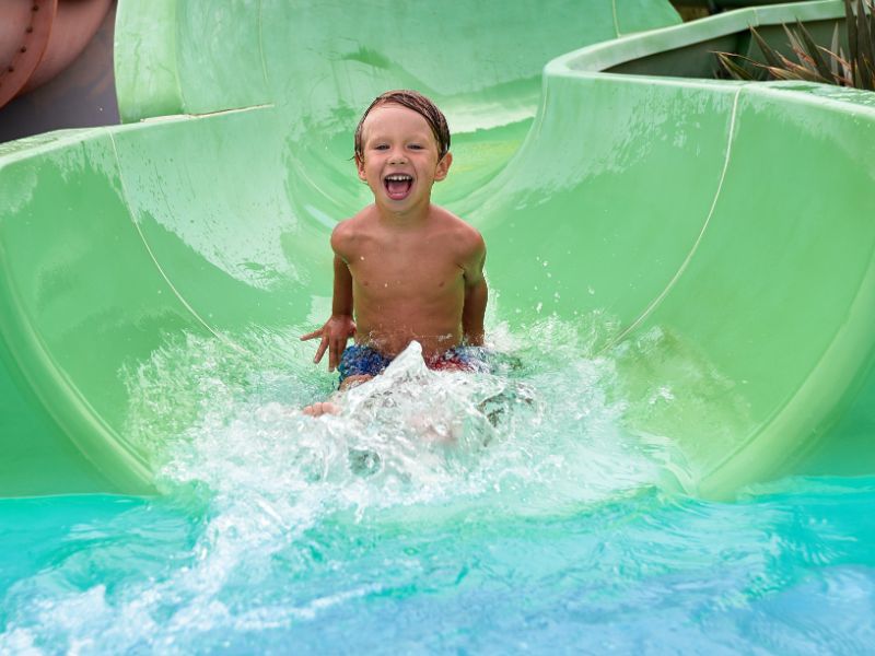 Fröhlicher Junge in einem Aquapark auf einer bunten Rutsche, mit Palmen im Hintergrund