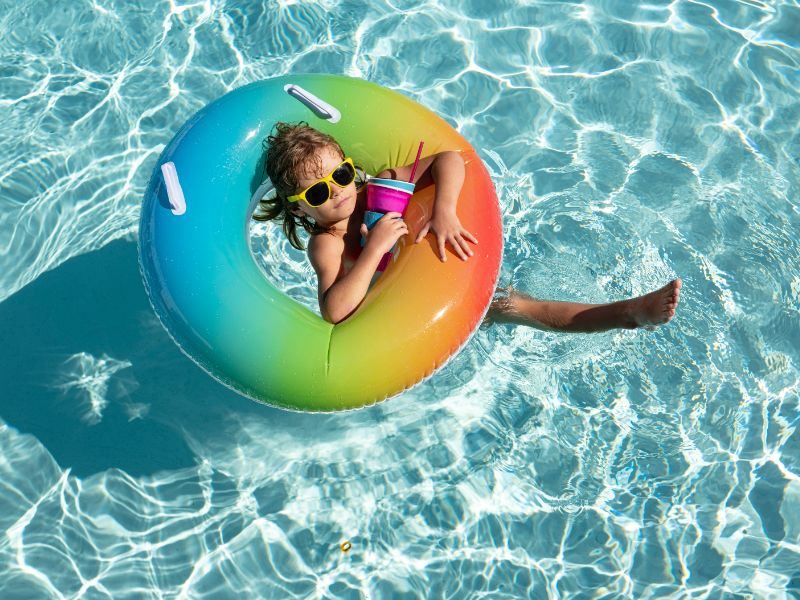 Kleines Mädchen treibt in bunten Schwimmring mit gelber Sonnenbrille im glasklaren Wasser.