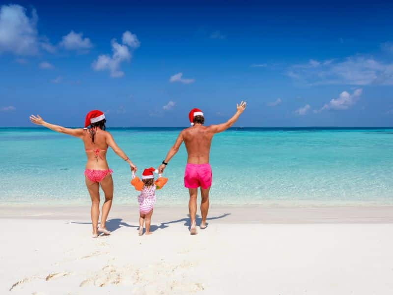 Mutter und Vater mit kleinem Mädchen an der Hand und Weihnachtmütze am feinen Sandstrand