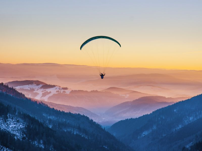 Paraglider schwebt über die schneebedeckten Gipfel dem Sonnenuntergang entgegen.