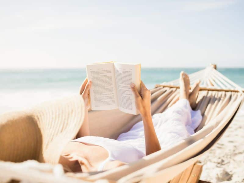 Frau am Strand in einer Hängematte, die entspannt ein Buch liest.