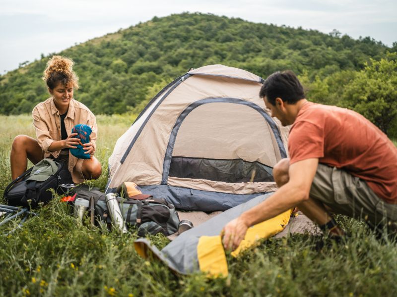 Junge Frau und junger Mann vor kleinem Zelt, am Aufräumen der Campingausrüstung