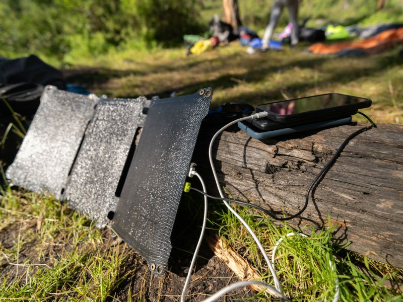 Smartphones auf einem Baumstamm, die von einer Powerbank mit Solarpanelen aufgeladen werden