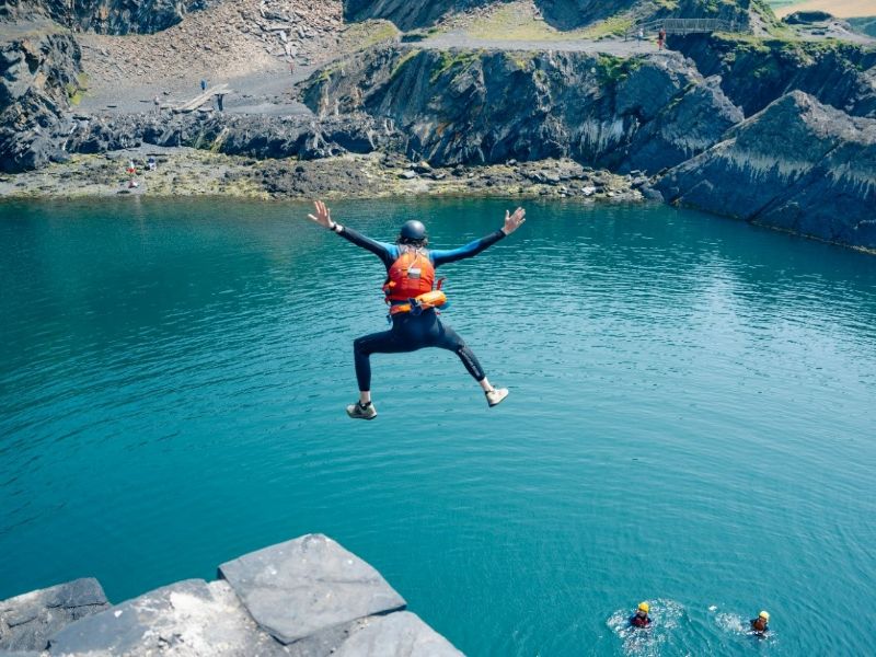 Person die von einer Klippe mit weit ausgestreckten Armen und Beinen springt