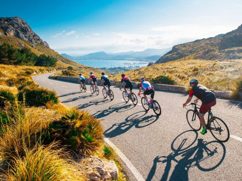 Gruppe Rennradfahrer, die eine hügelige Straße hinabfahren und einen Ausblick auf die Küste der Costa Brava haben.